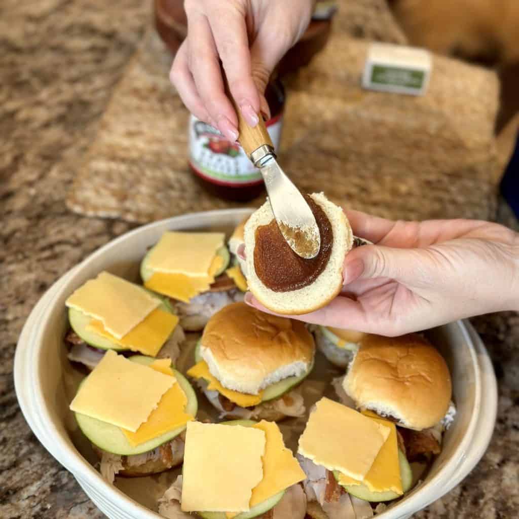 Spreading apple butter on the top of a slider bun.