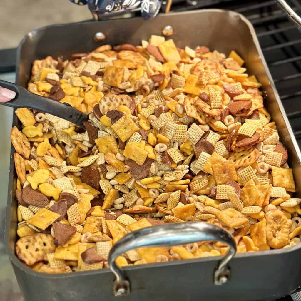 Stirring chex mix in a roaster in the oven.