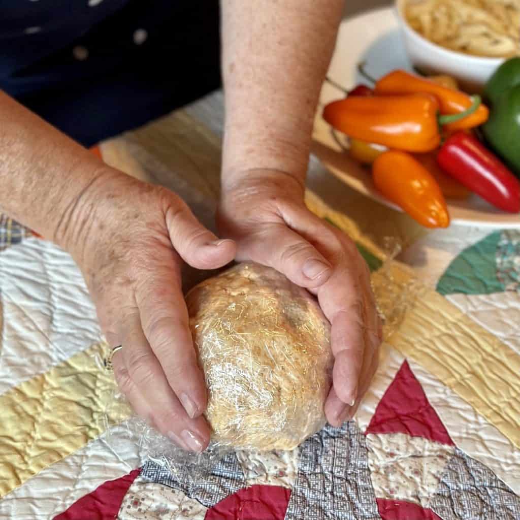 Shaping a cheeseball into a ball in plastic wrap.