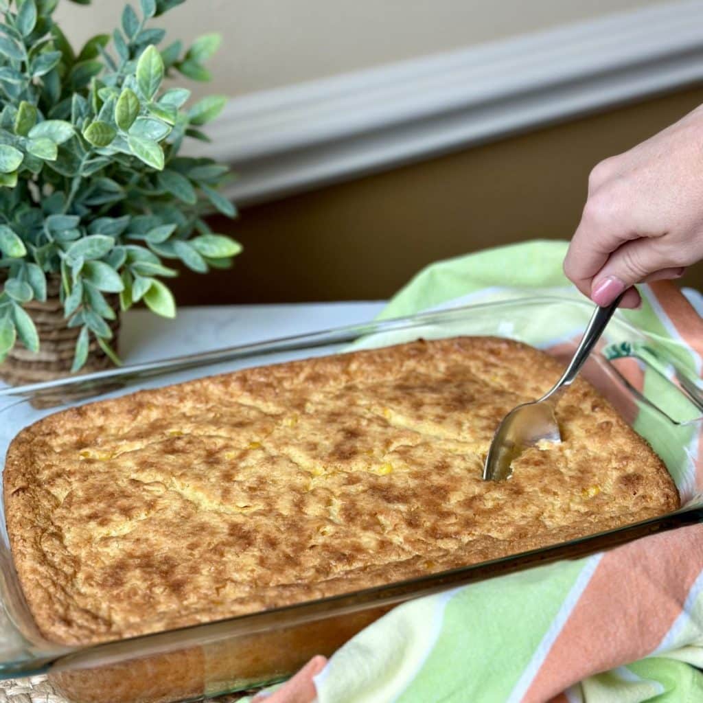 A spoon dipping brown and yellow corn casserole out of a baking dish