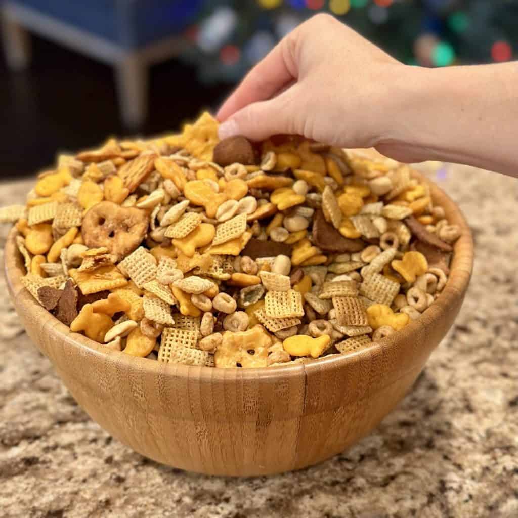 A person’s hand getting a bite of chex party mix.