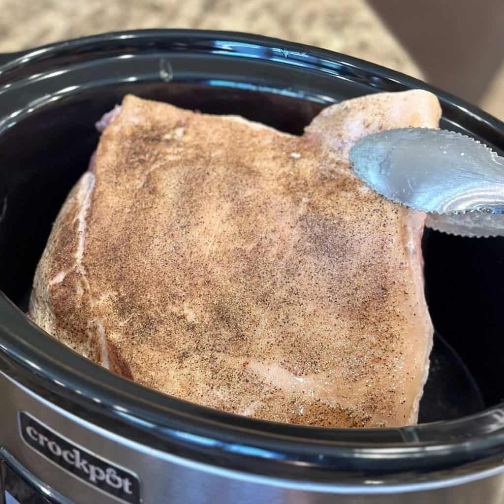 Adding a pork butt to a crockpot.