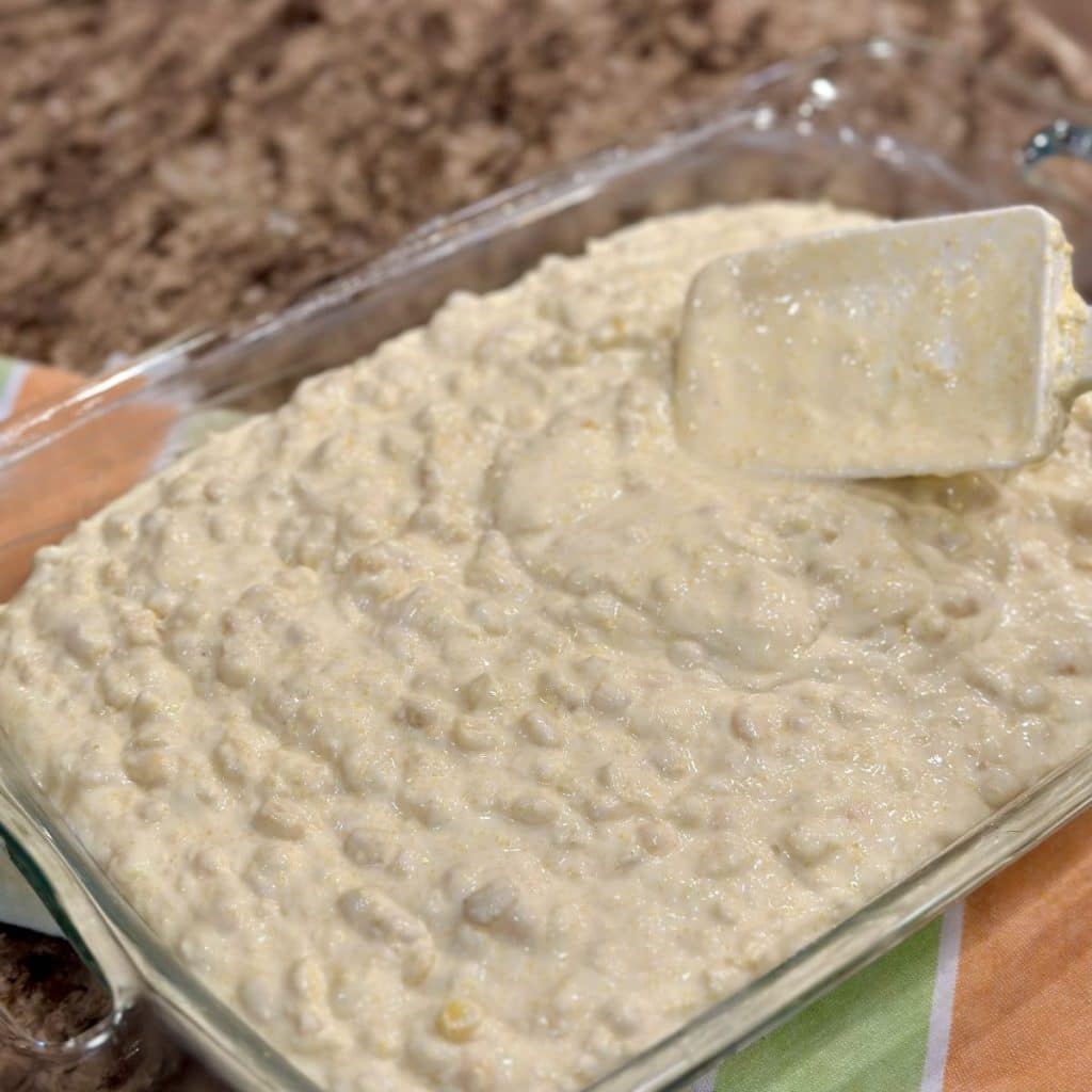 Country scalloped corn mixture of ingredients being spread in a baking dish.