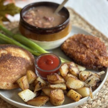 A plate with soup beans, hoecakes, a pork chop, and fried potatoes and onions.