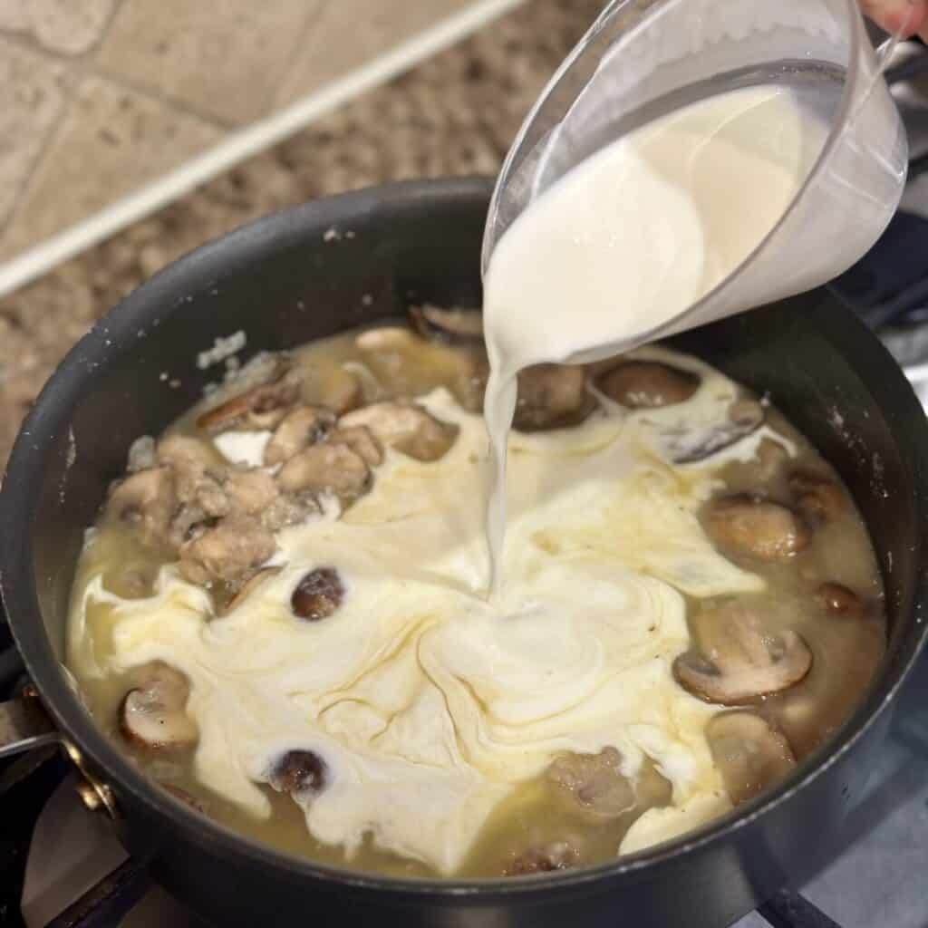 Adding cream to the filling of turkey tetrazzini in a pan.