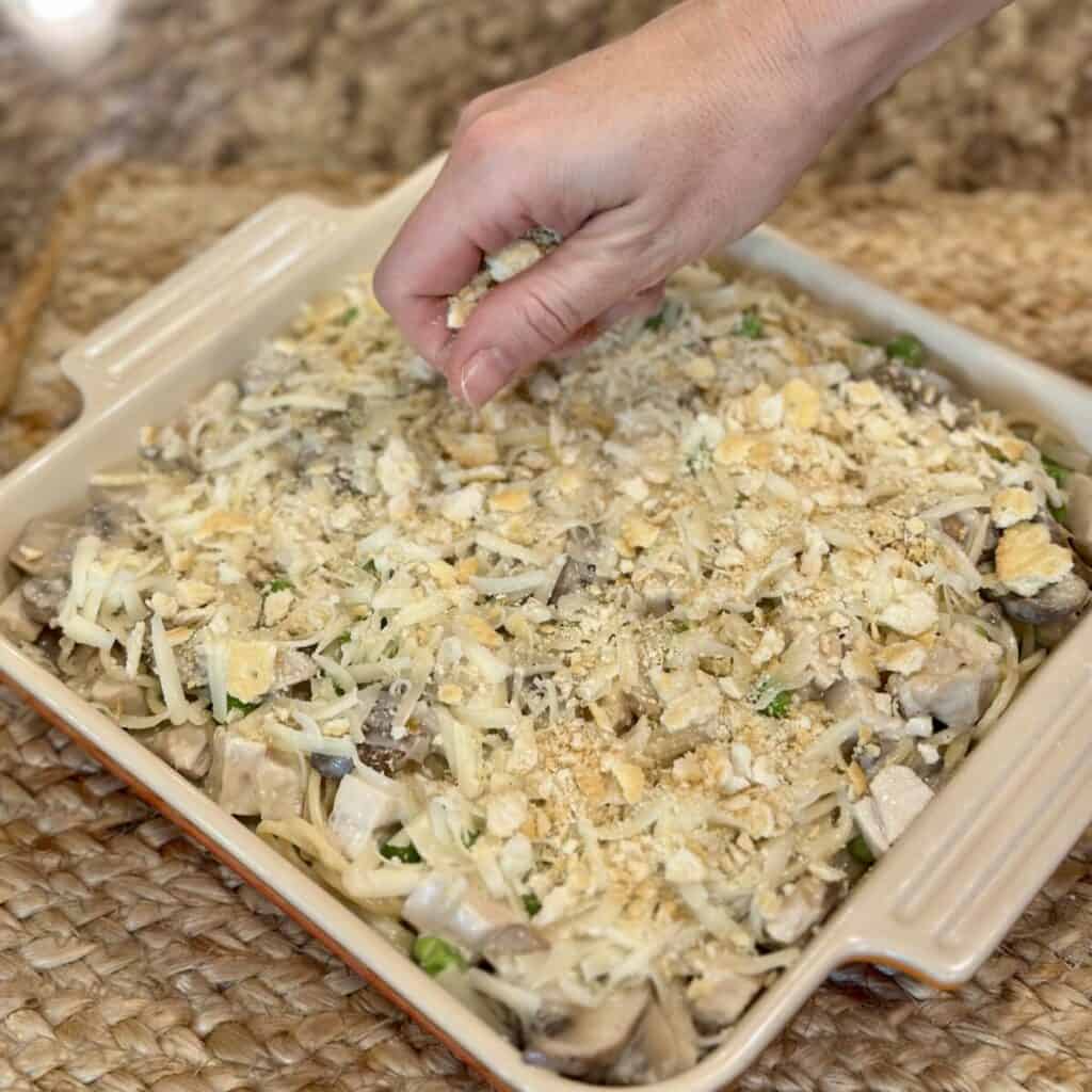 Adding crackers and cheese to the top of turkey tetrazzini.