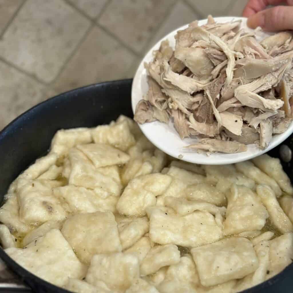 Adding chicken to dumplings in a pot.