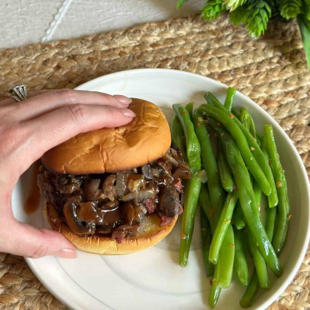 A sandwich next to cooked green beans on a plate.