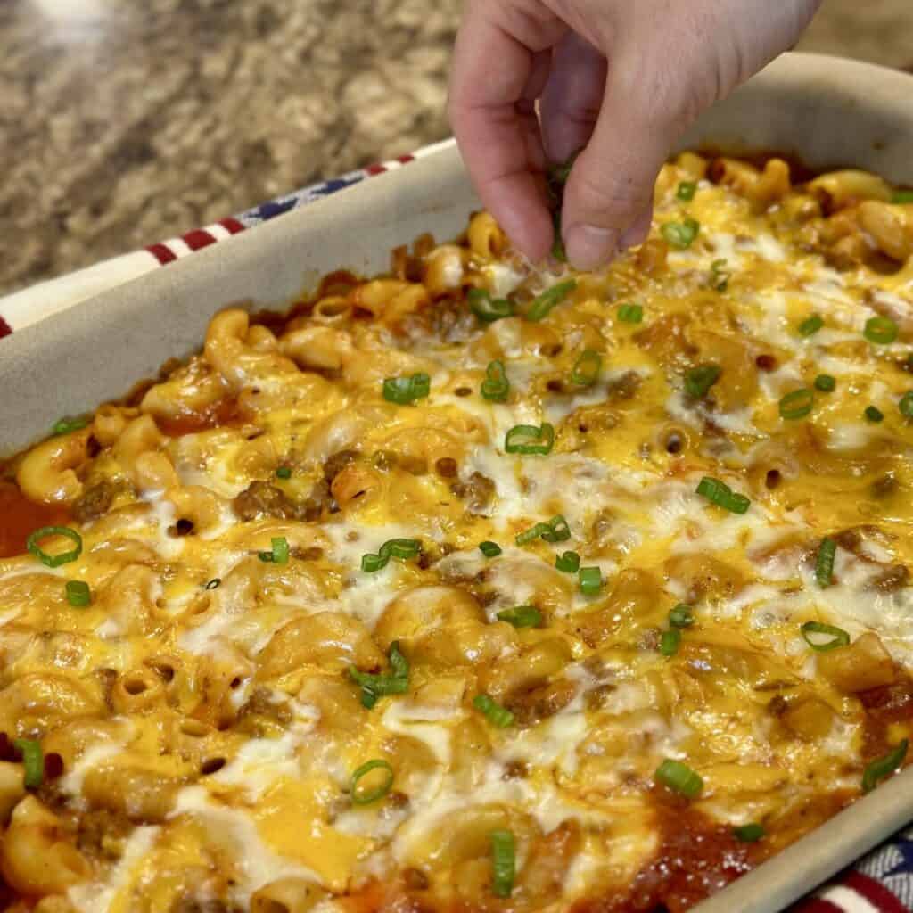 Adding green onions to the top of beef Mac and cheese.