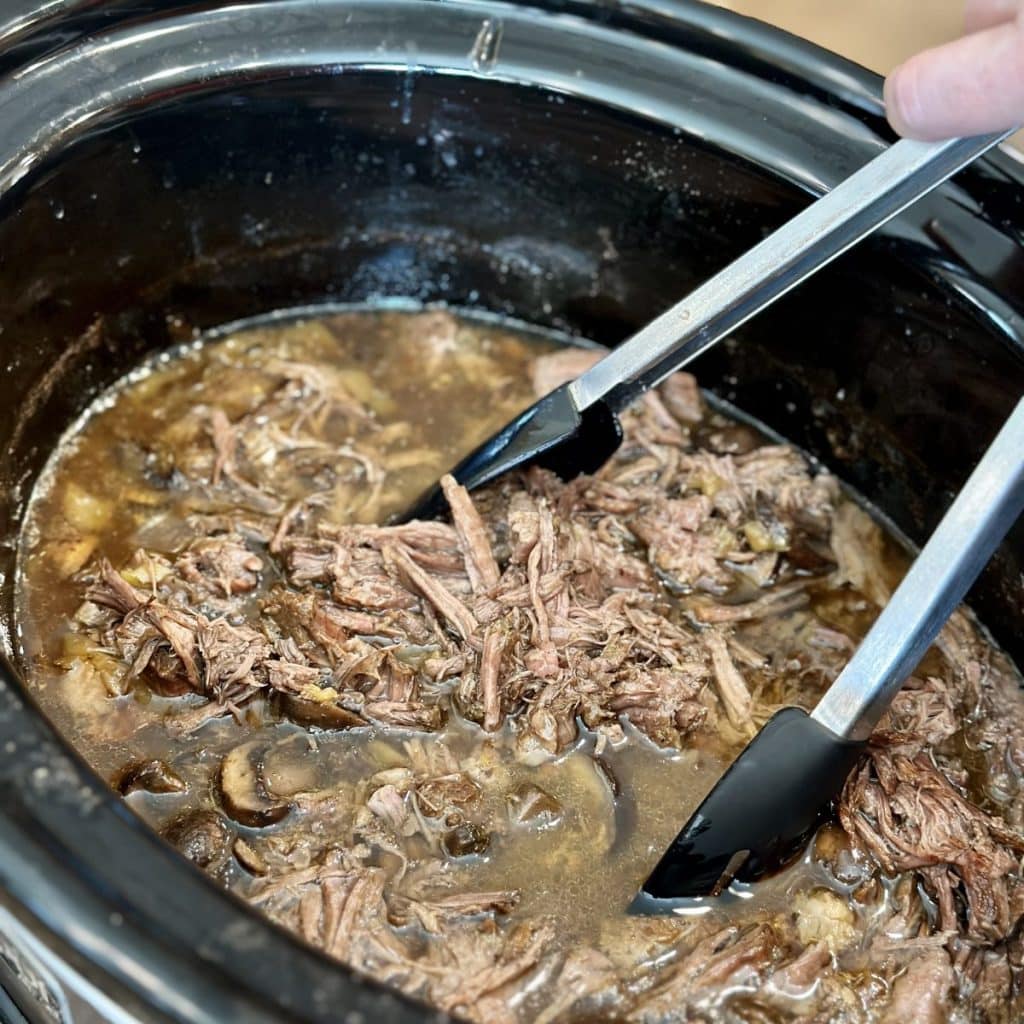 Shredded seasoned roast in a crockpot.