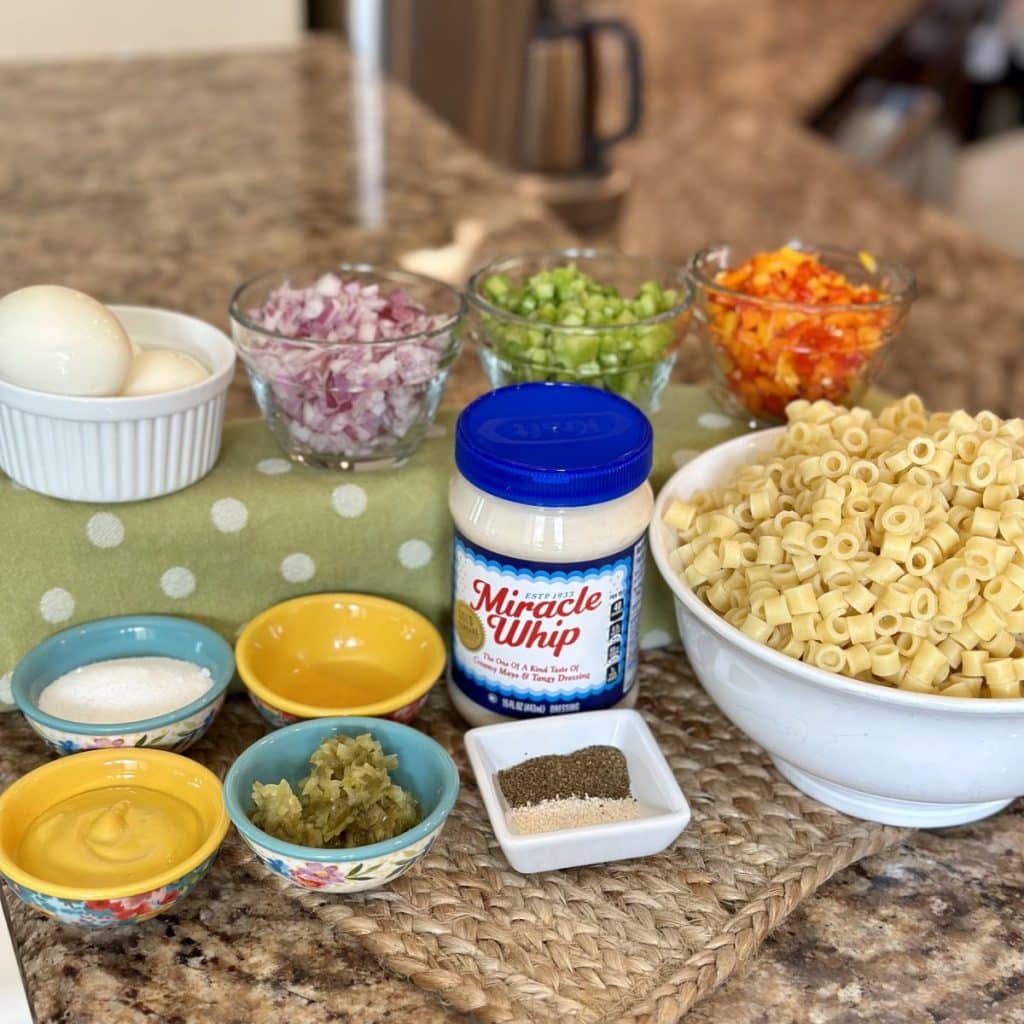 Ingredients to make a salad: miracle whip, sugar, celery seed, garlic salt, apple cider vinegar, dill pickle relish, yellow mustard, pasta, eggs, red onion, celery and bell peppers.