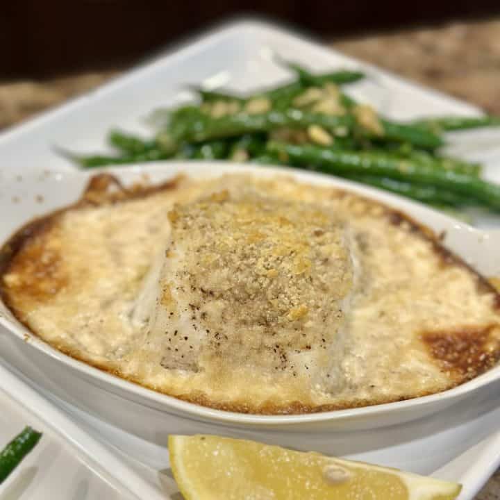 A baked cod in cream sauce on a plate.