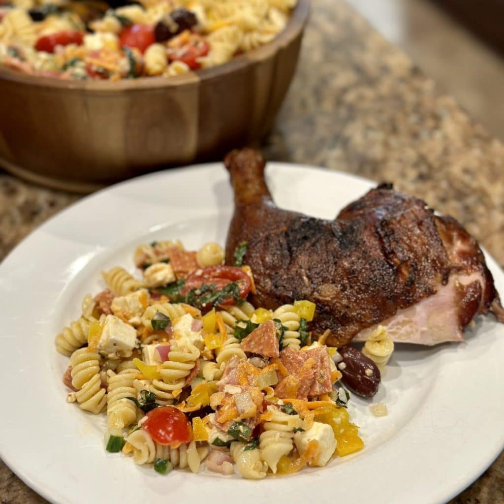 Pasta salad next to a chicken leg quarter on a plate.