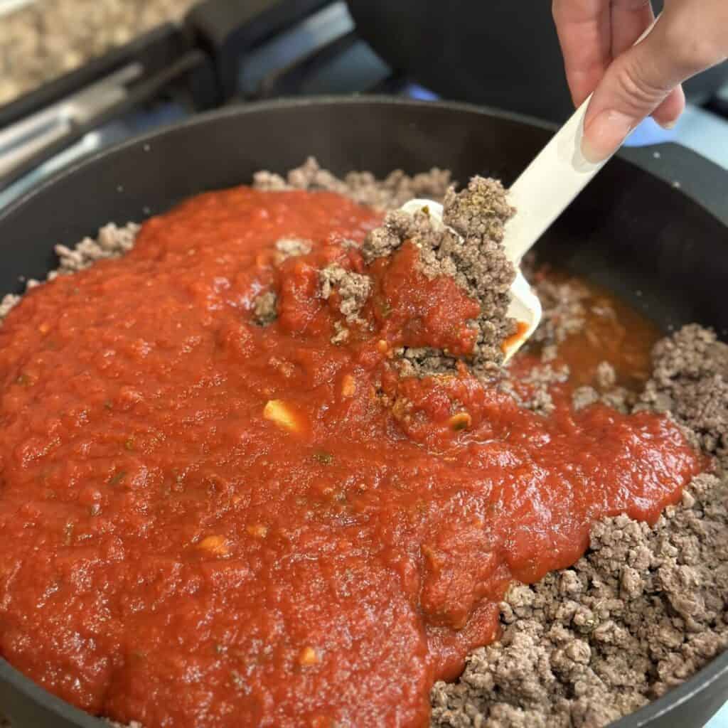 Stirring marinara sauce in beef in a skillet.