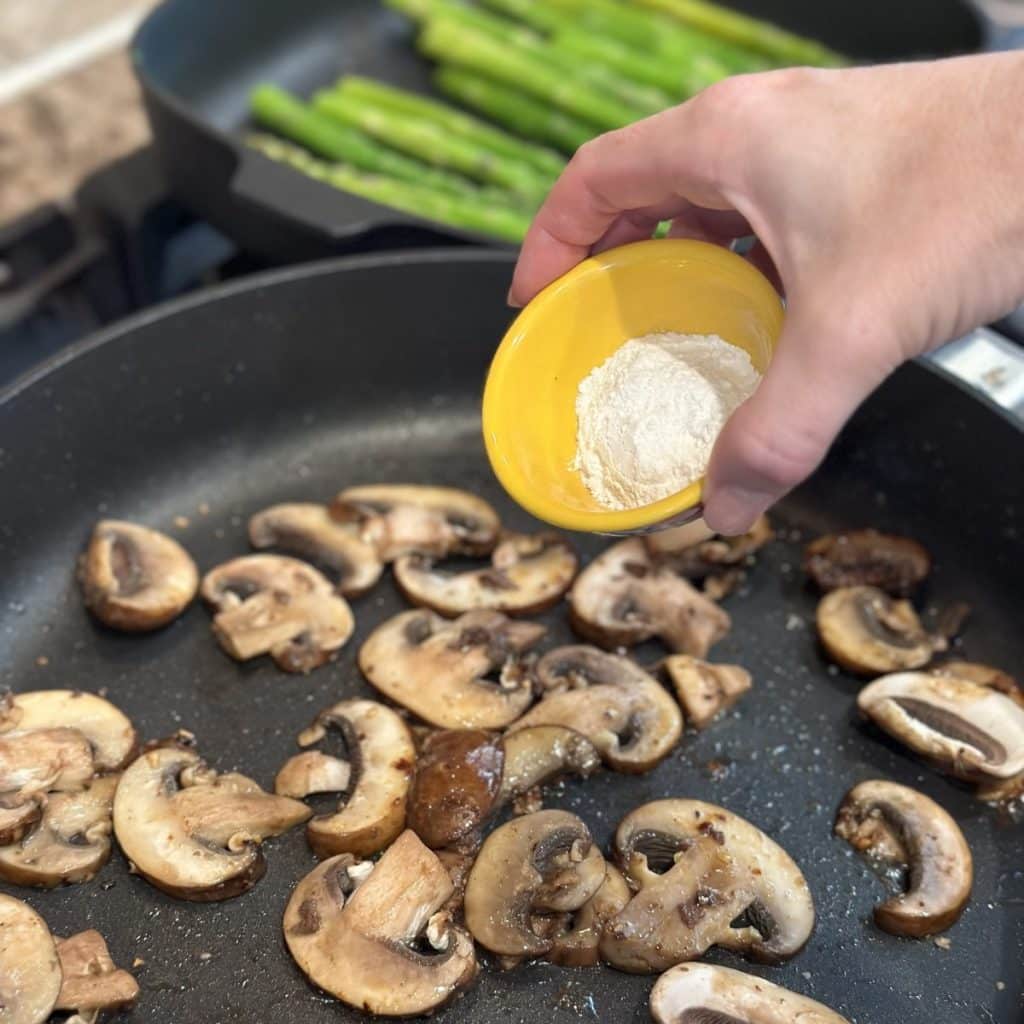 Adding flour to a pan of mushrooms.