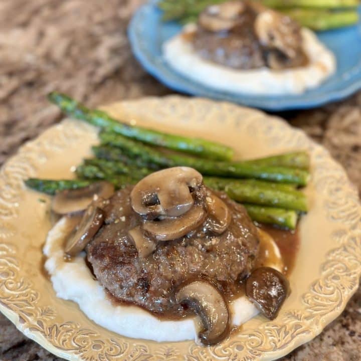 A plate with mashed potatoes, hamburger steaks, mushrooms and asparagus.