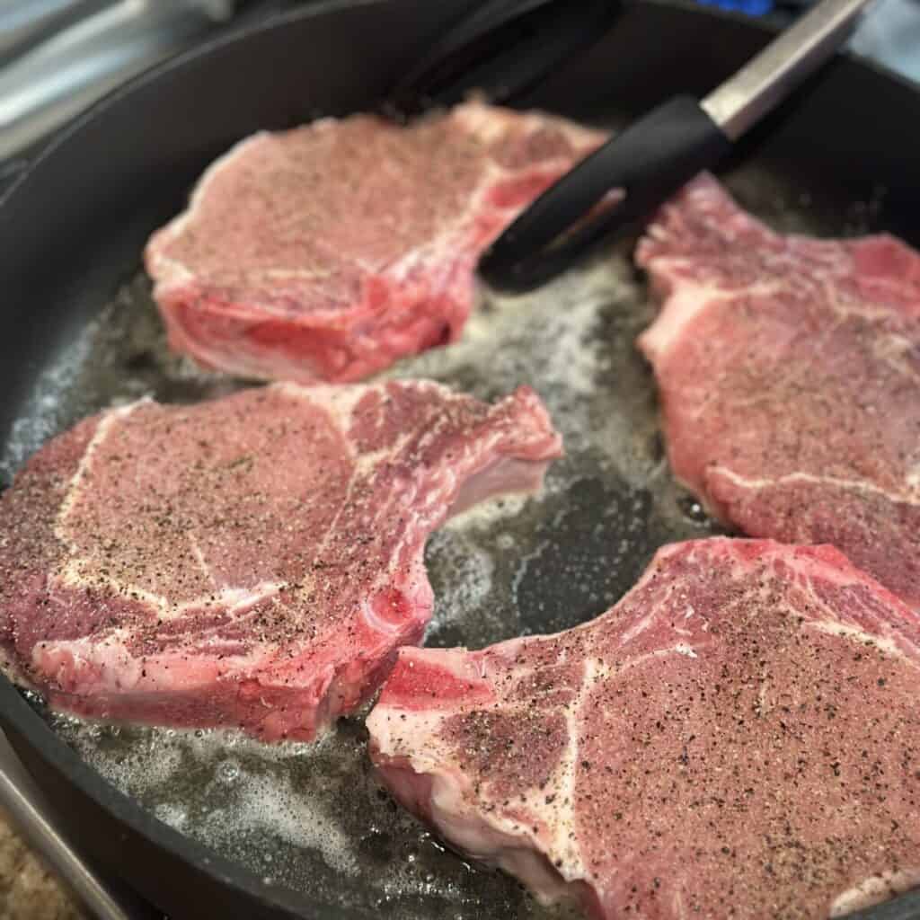 Searing pork chops in a skillet.