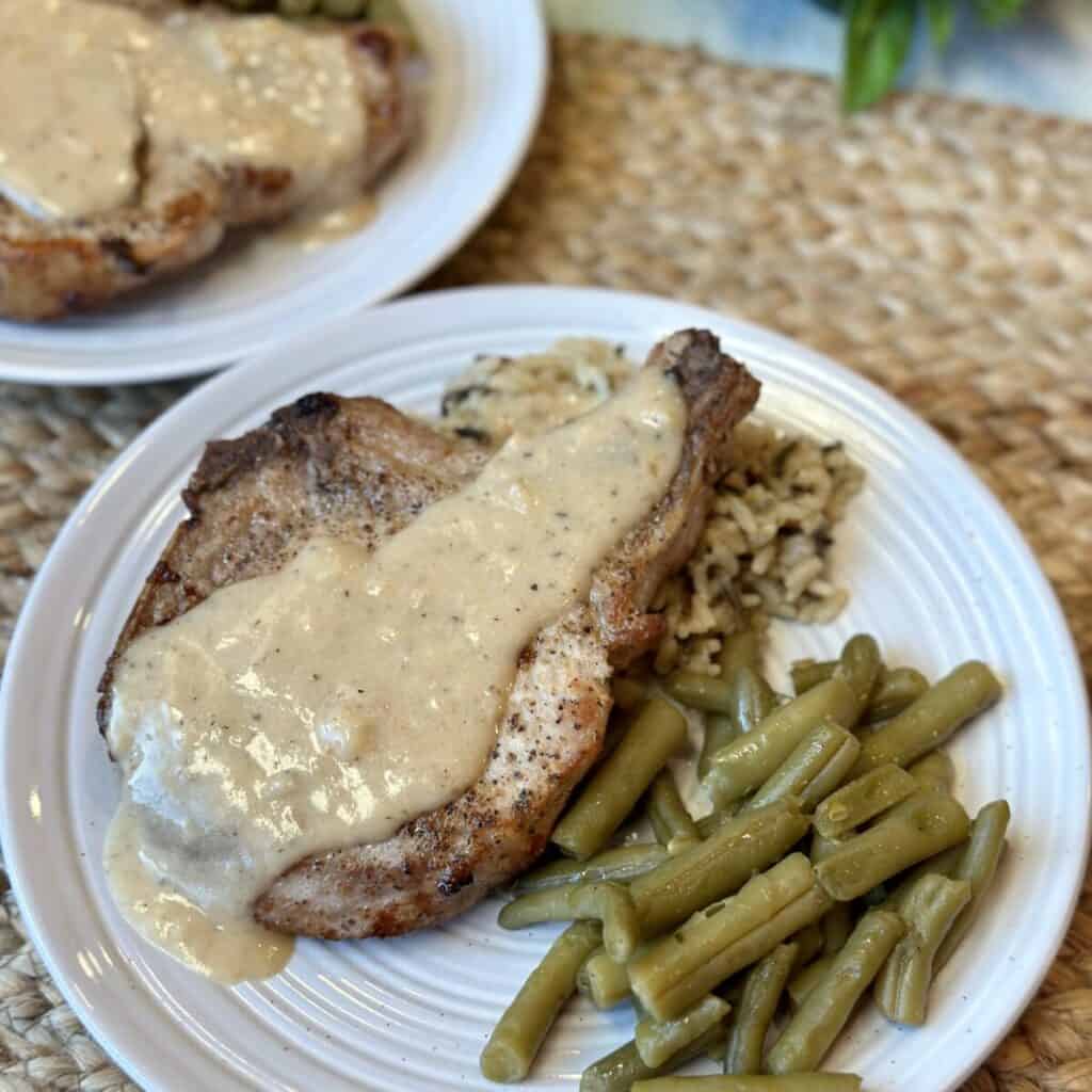 A gravy topped pork chop on a plate with green beans and rice.