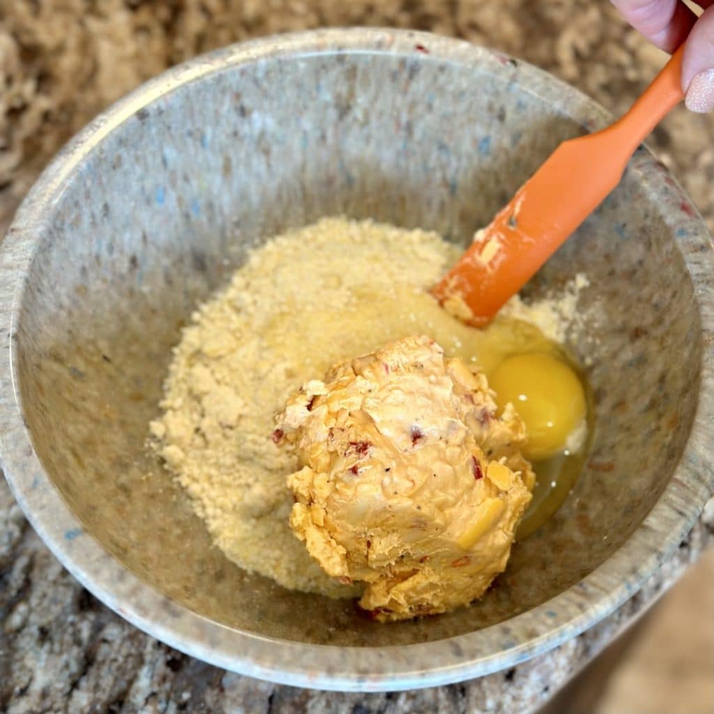 A bowl with sweet cornbread mix, pimento cheese and an egg.