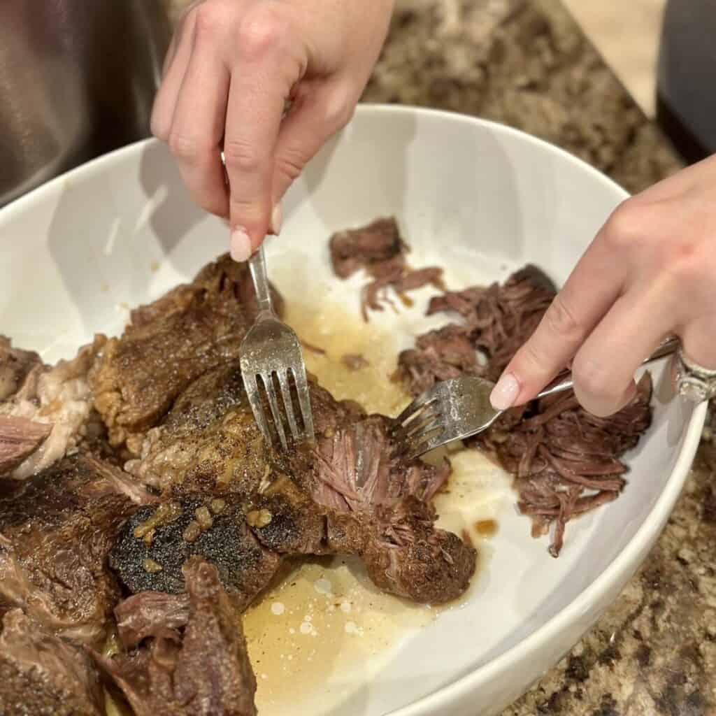 Shredding a cooked roast beef.