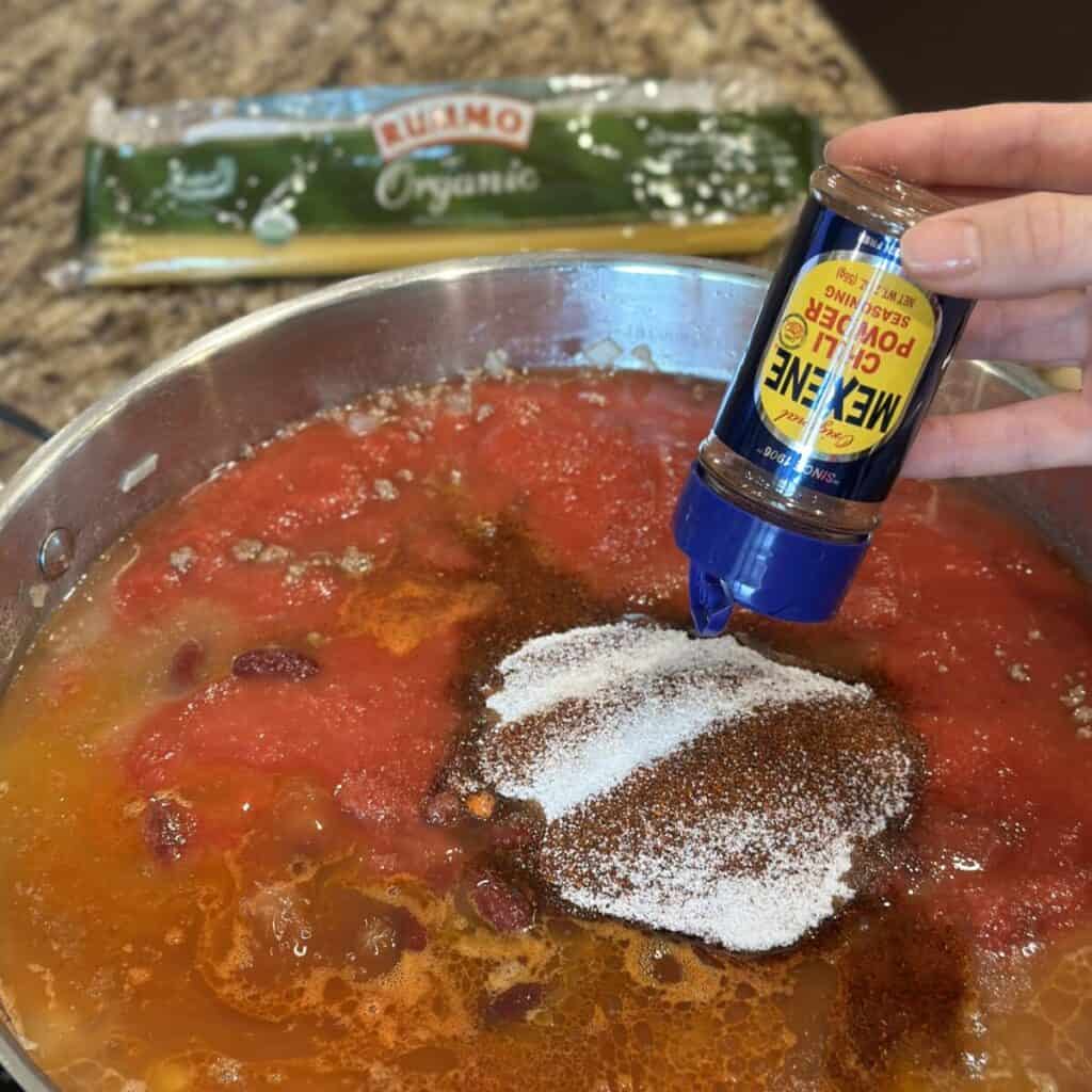 Adding chili powder to chili in a pan.