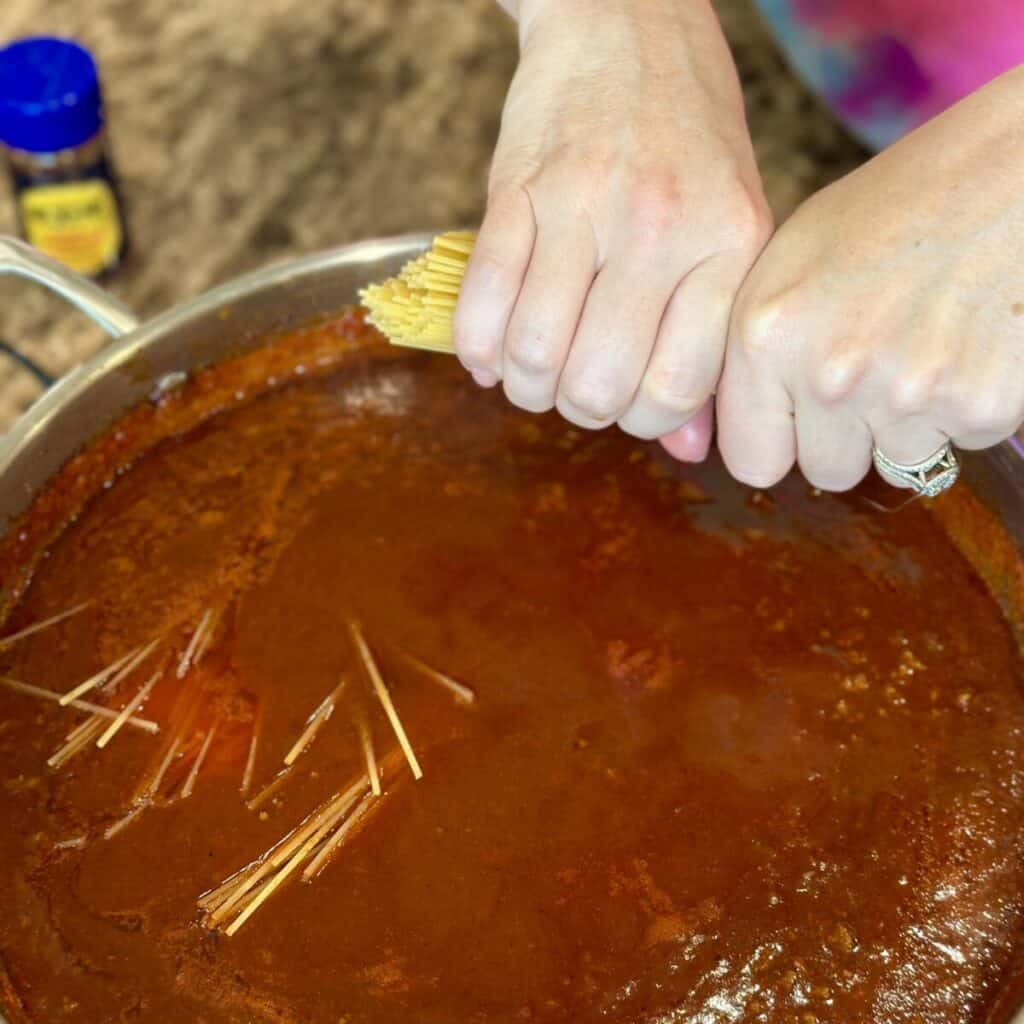 Adding spaghetti to a pan of chili.