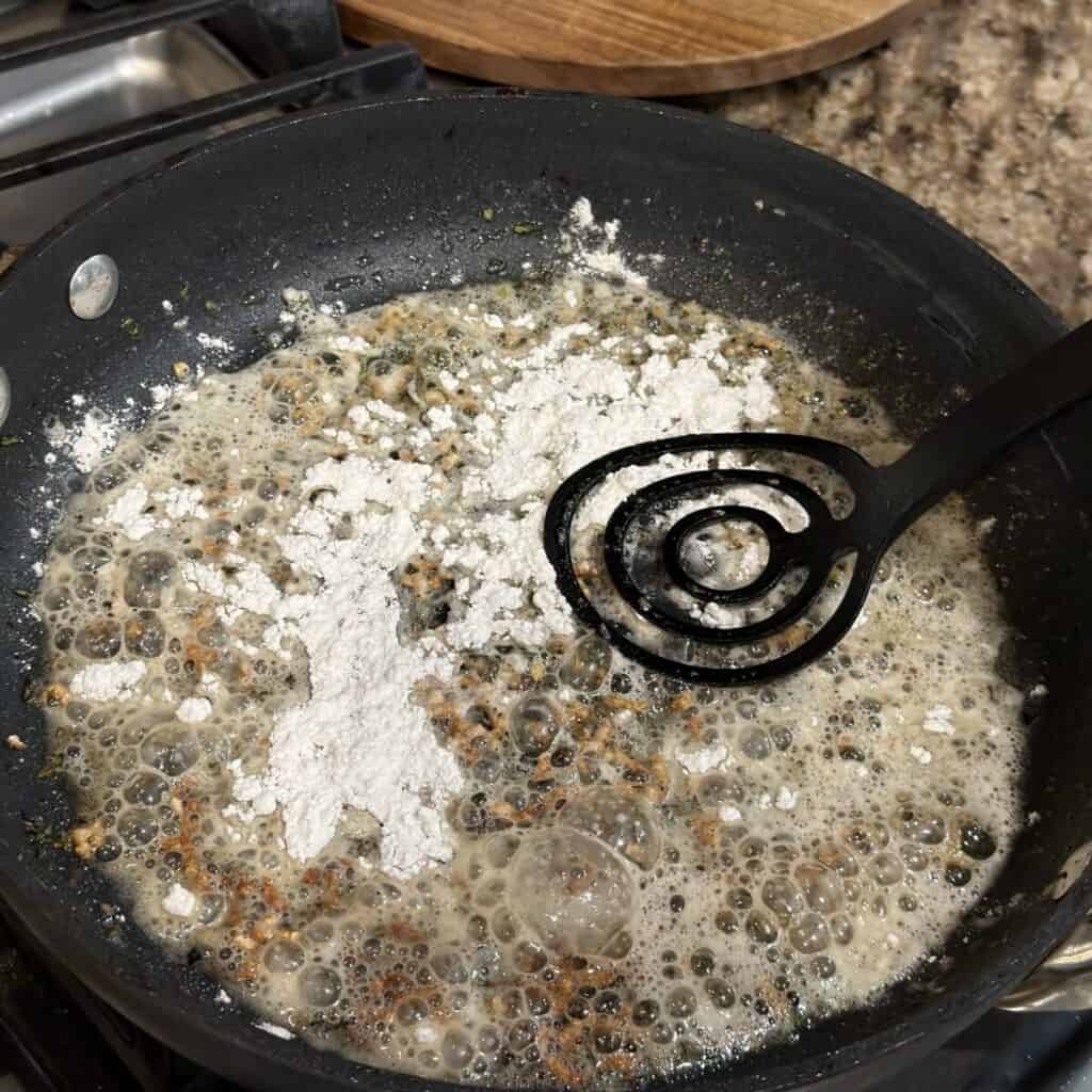 Adding flour to butter and herbs in a skillet for gravy.