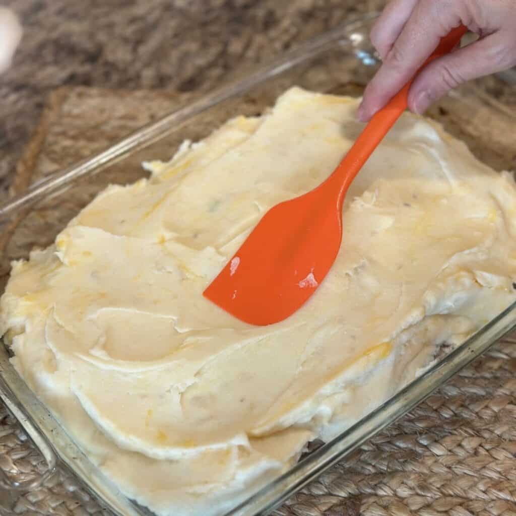 Spreading mashed potatoes on top of meatloaf.