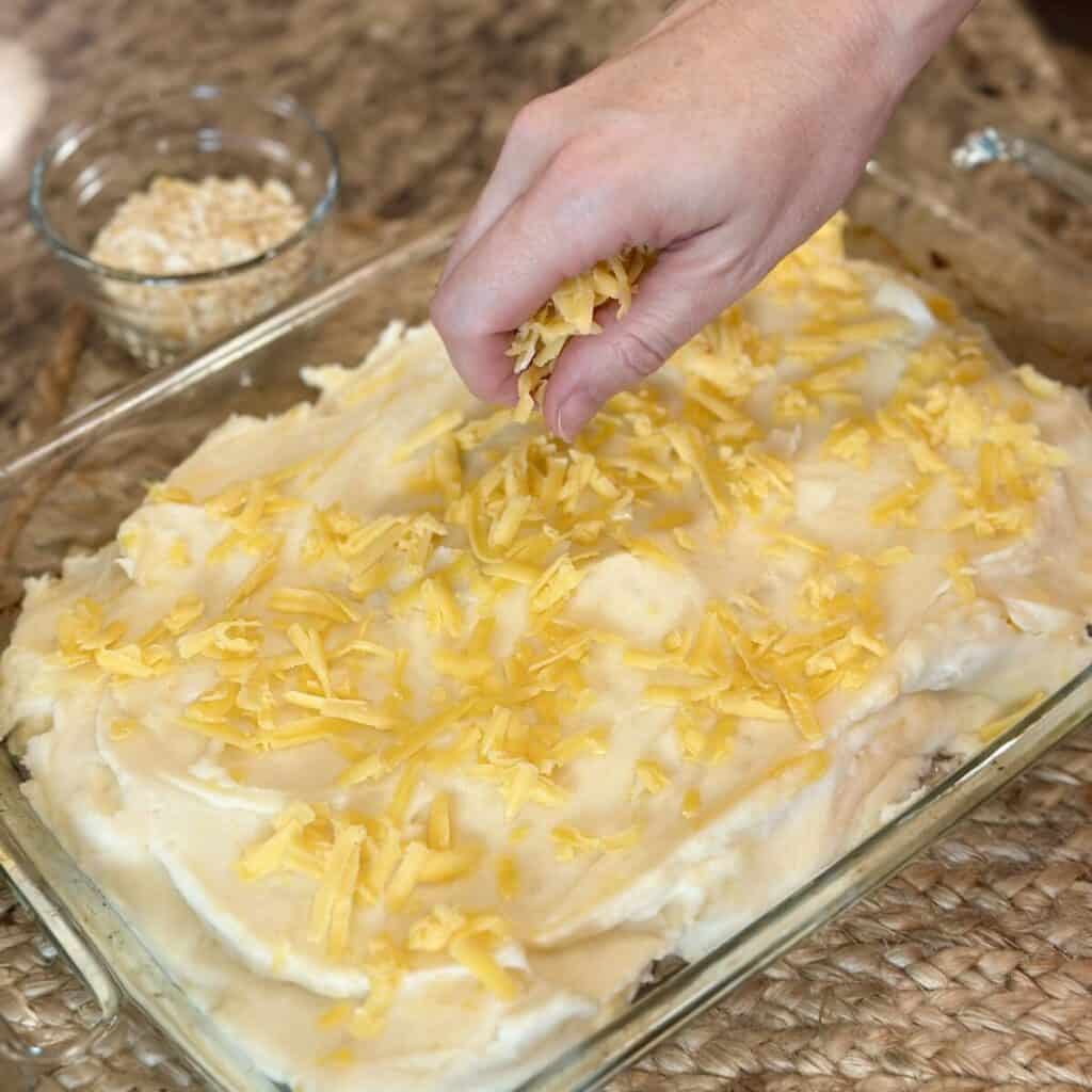 Adding cheese to the top of meatloaf casserole.