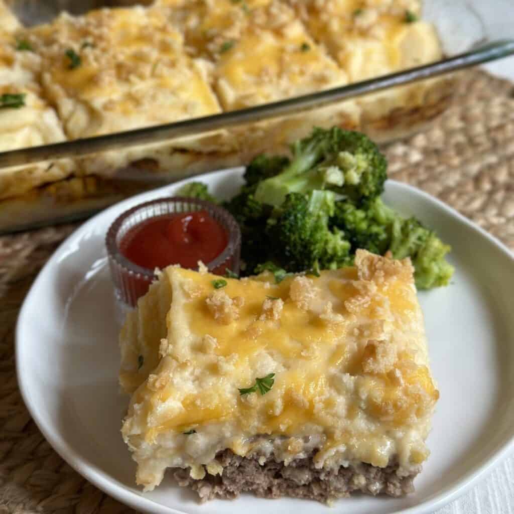 A serving of meatloaf casserole on a plate with broccoli.