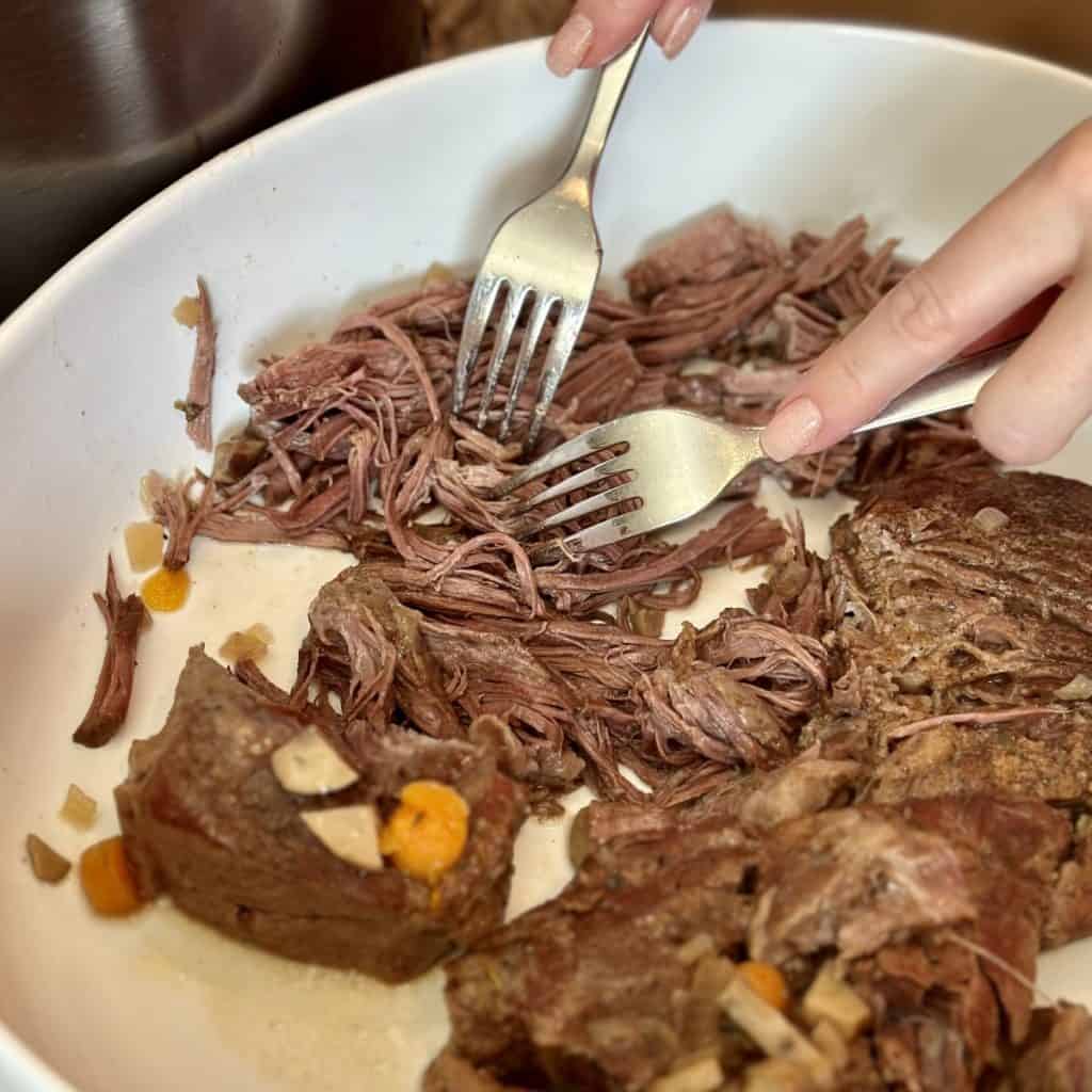 Shredding chuck roast in a bowl.