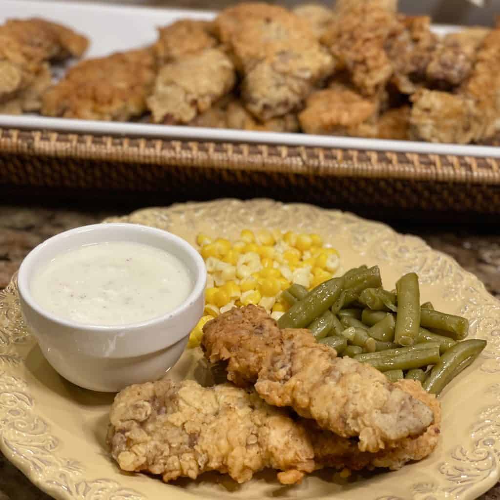 completed cube steak fingers served on a plate with country gravy, corn, and green beans