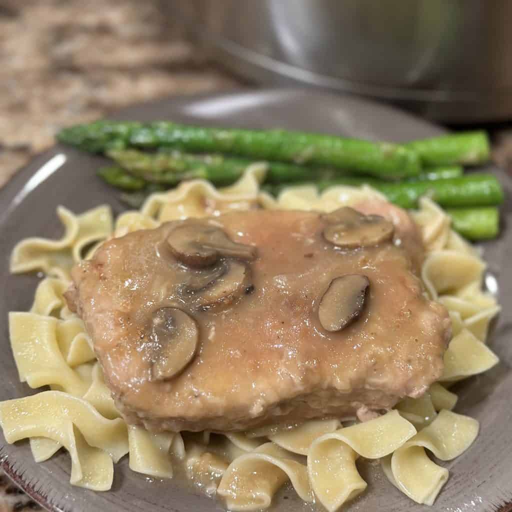 a smothered porkchop with brown gravy and mushrooms served over noodles