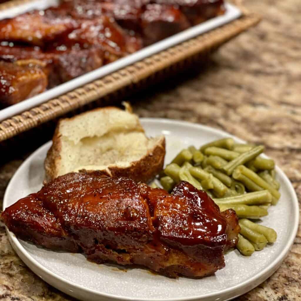 A plate of country style bbq ribs, green beans and a potato.