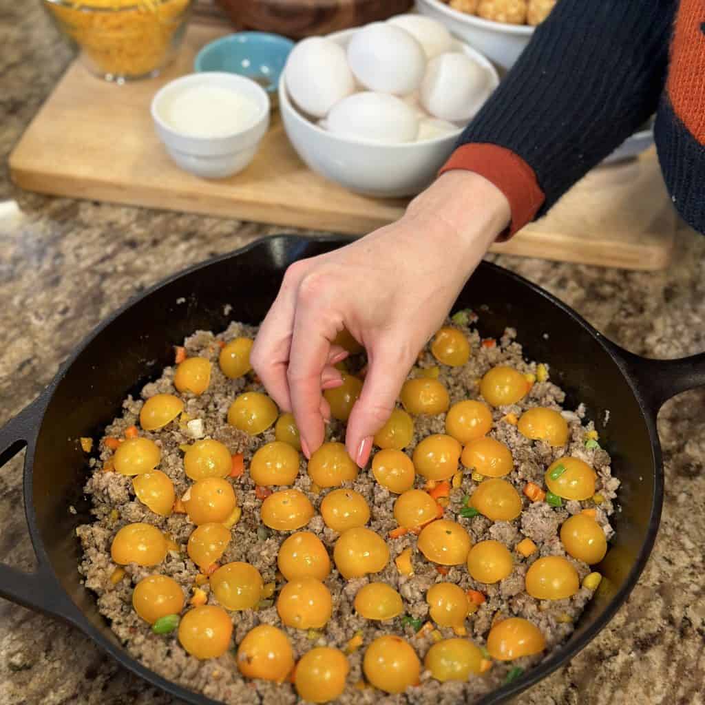 placing the tomato halves in the sausage and vegetable mix in a pan