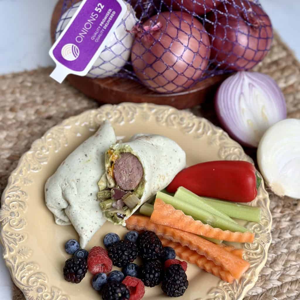 sausage and onion in a tortilla wrap with fresh fruit and vegetables on the side 