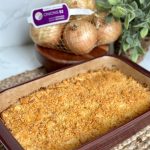 This is a picture of a casserole in a maroon dish. The casserole contains onions and is topped with a cheesy toasted yellow cracker crumb.