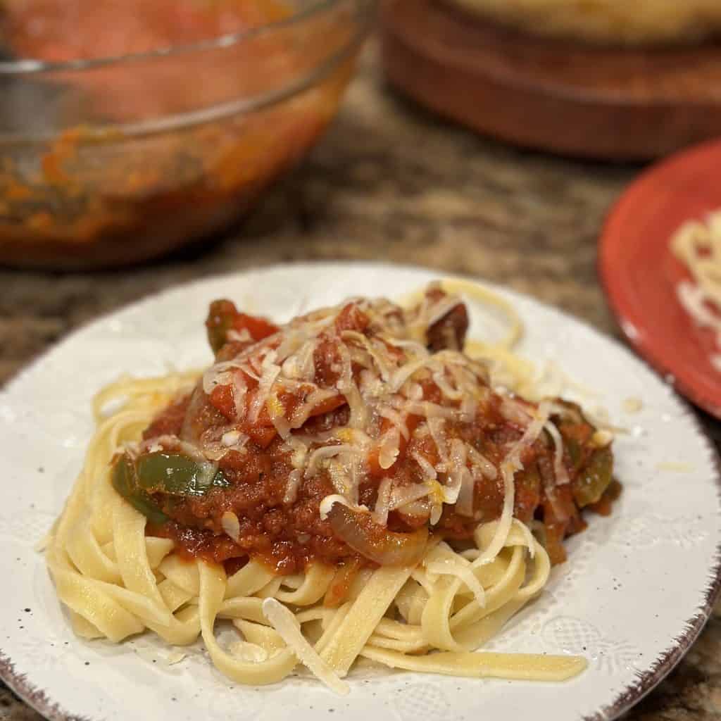 a plate of sausage and pepper pasta with red sauce and shredded cheese on top