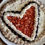 This is a picture of a large round brownie. It is decorated with whipped cream and a strawberry made with strawberries and cherries.