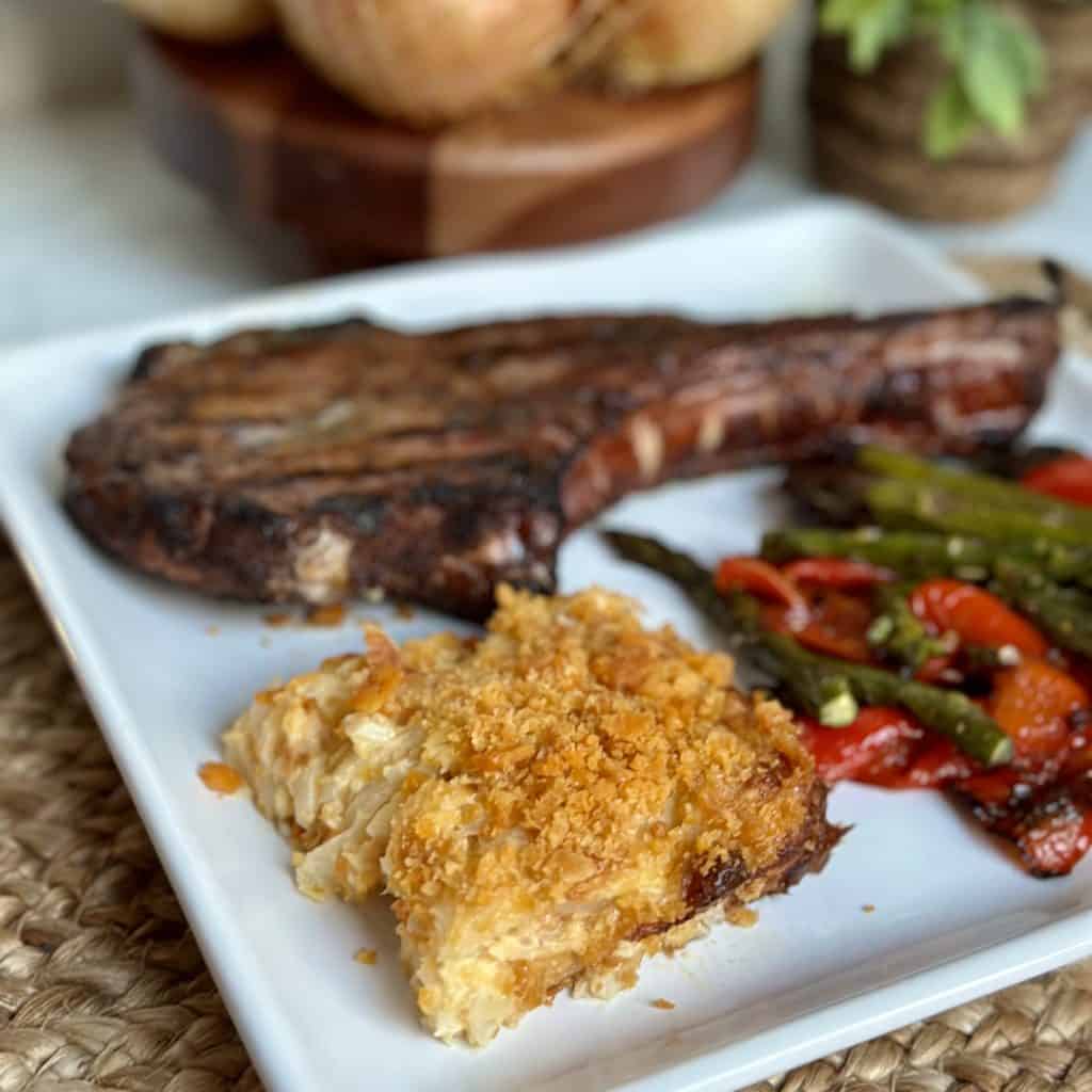 onion casserole on a dish with a steak and vegetables