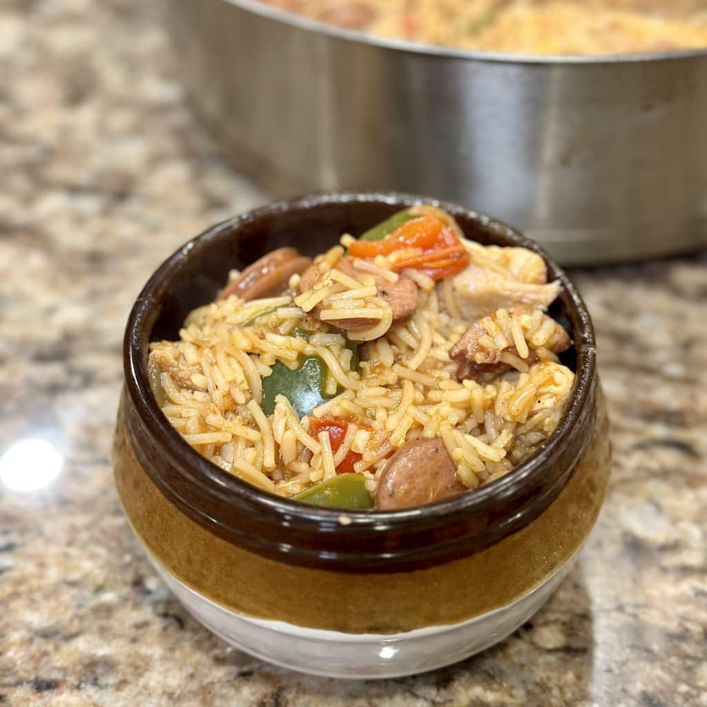 a bowl filled with a seasoned pasta and rice blend, sliced sausage and cooked red and green peppers and onions