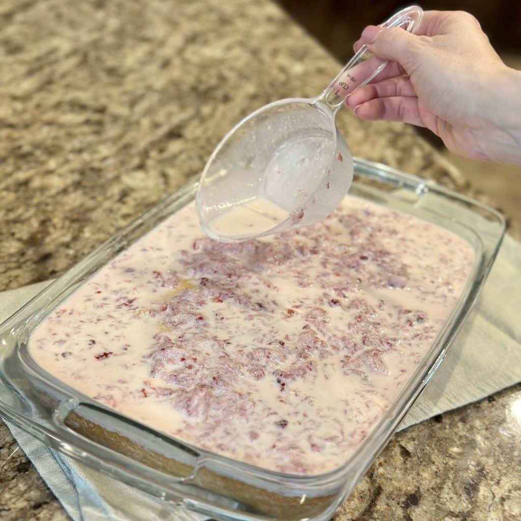 A mixture of 3 milk and mashed strawberries being poured over vanilla cake