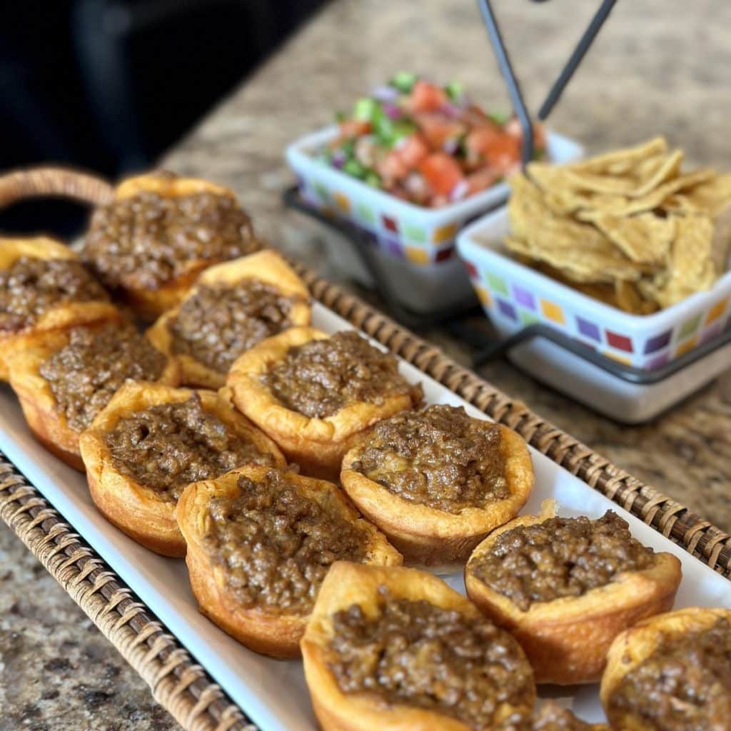 A tray of filled taco cups filled with chips and pico de Gallo on the side