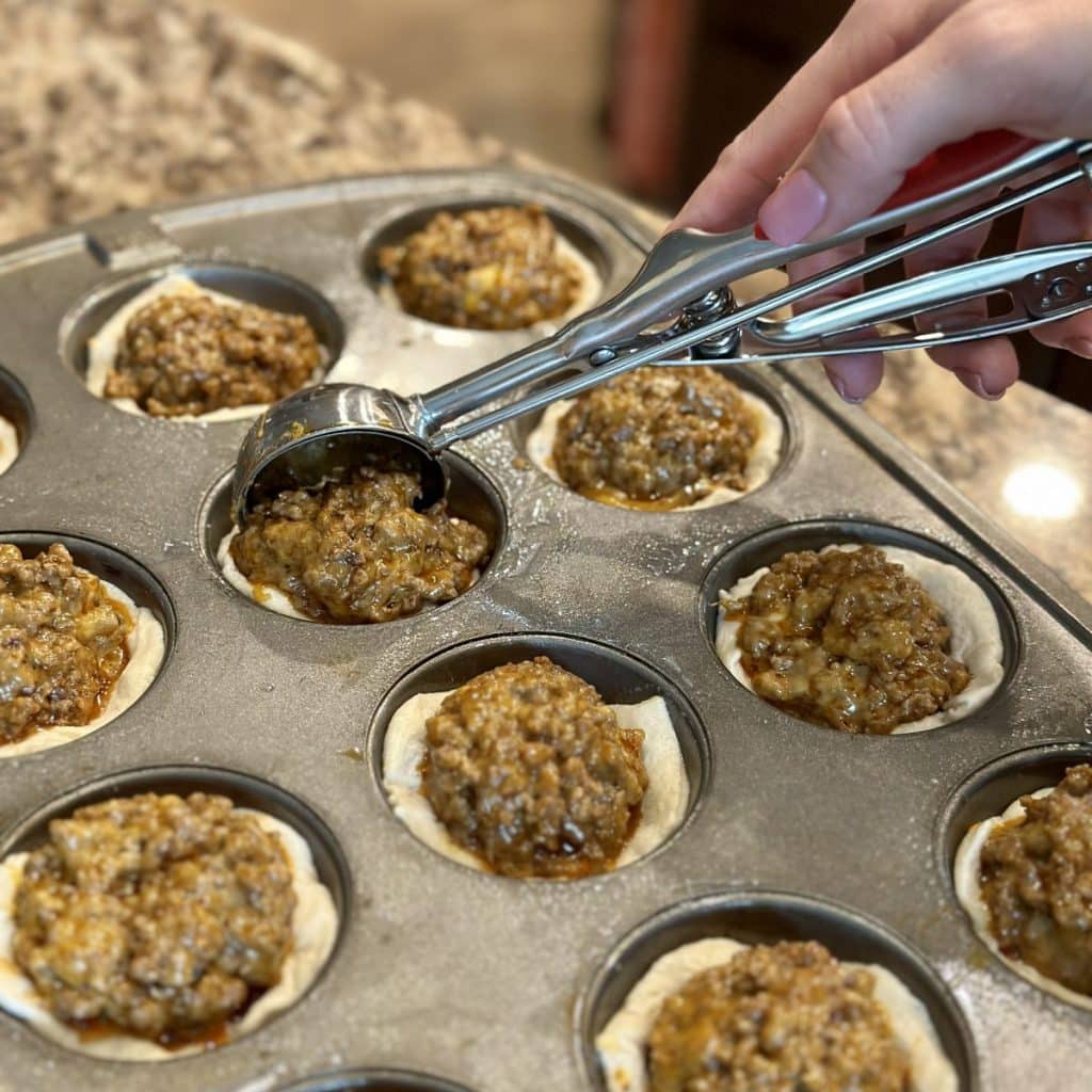 Using a scoop to fill biscuit dough crust with taco mix