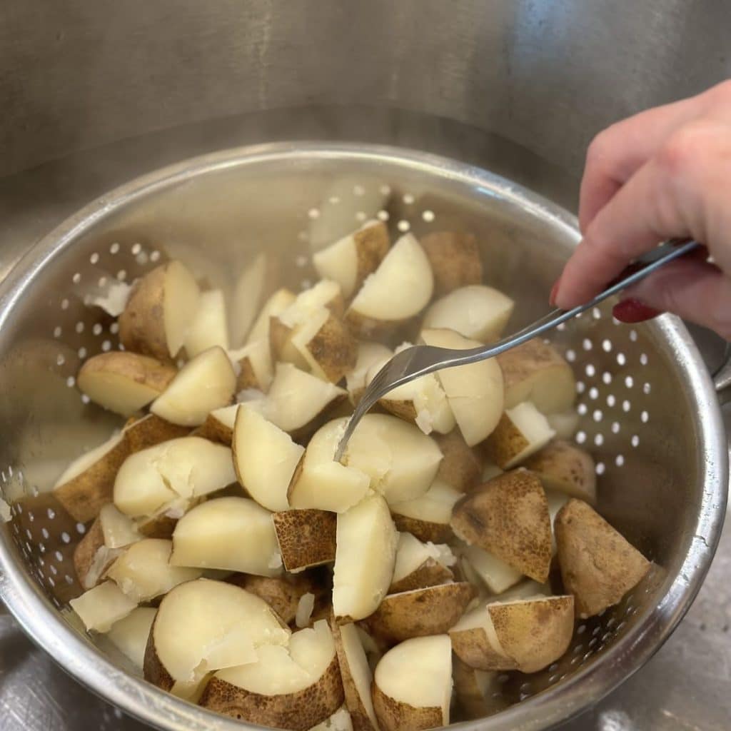 Potatoes drained in a colander and pierced with a fork to check tenderness