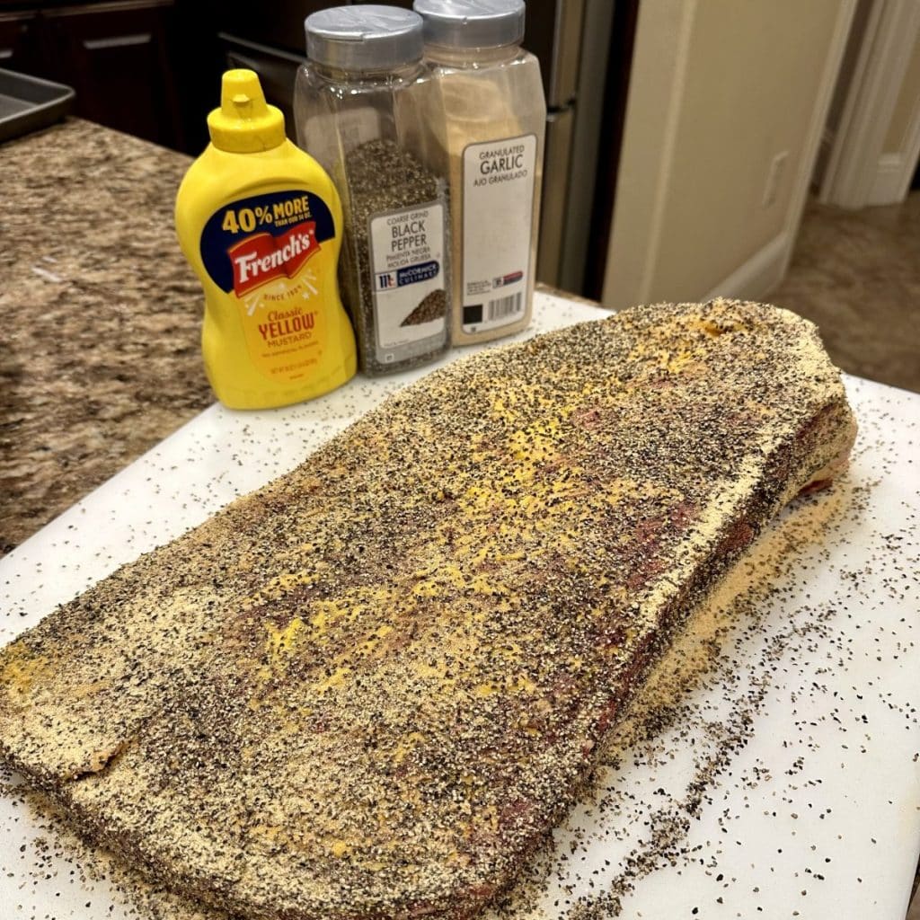 A seasoned brisket on a cutting board ready to be smoked.