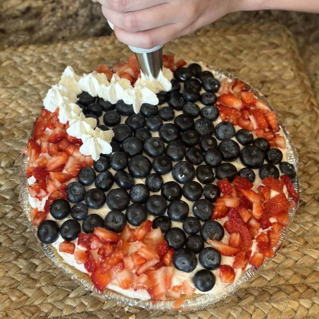 Adding whipped cream on top of a berry pie.