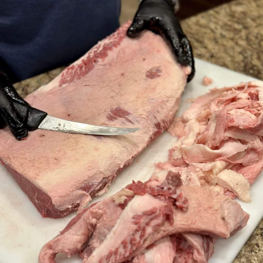 Trimming a brisket on a cutting board.