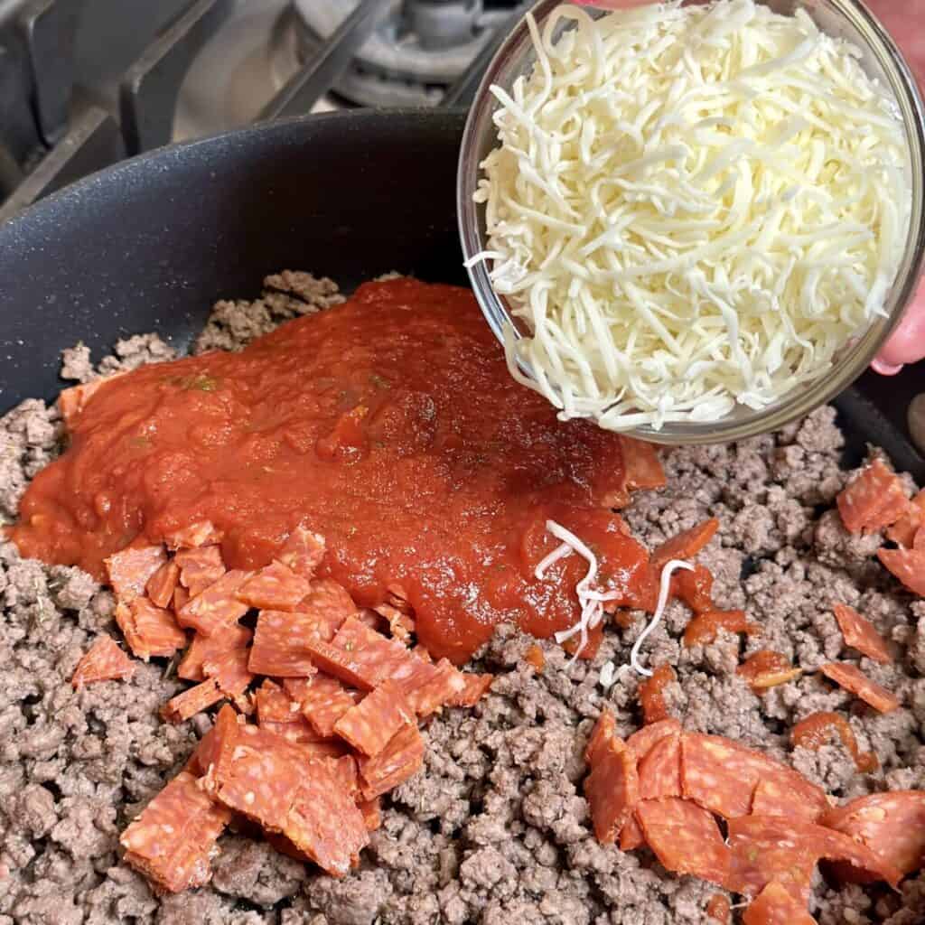 Adding cheese to beef in a skillet.