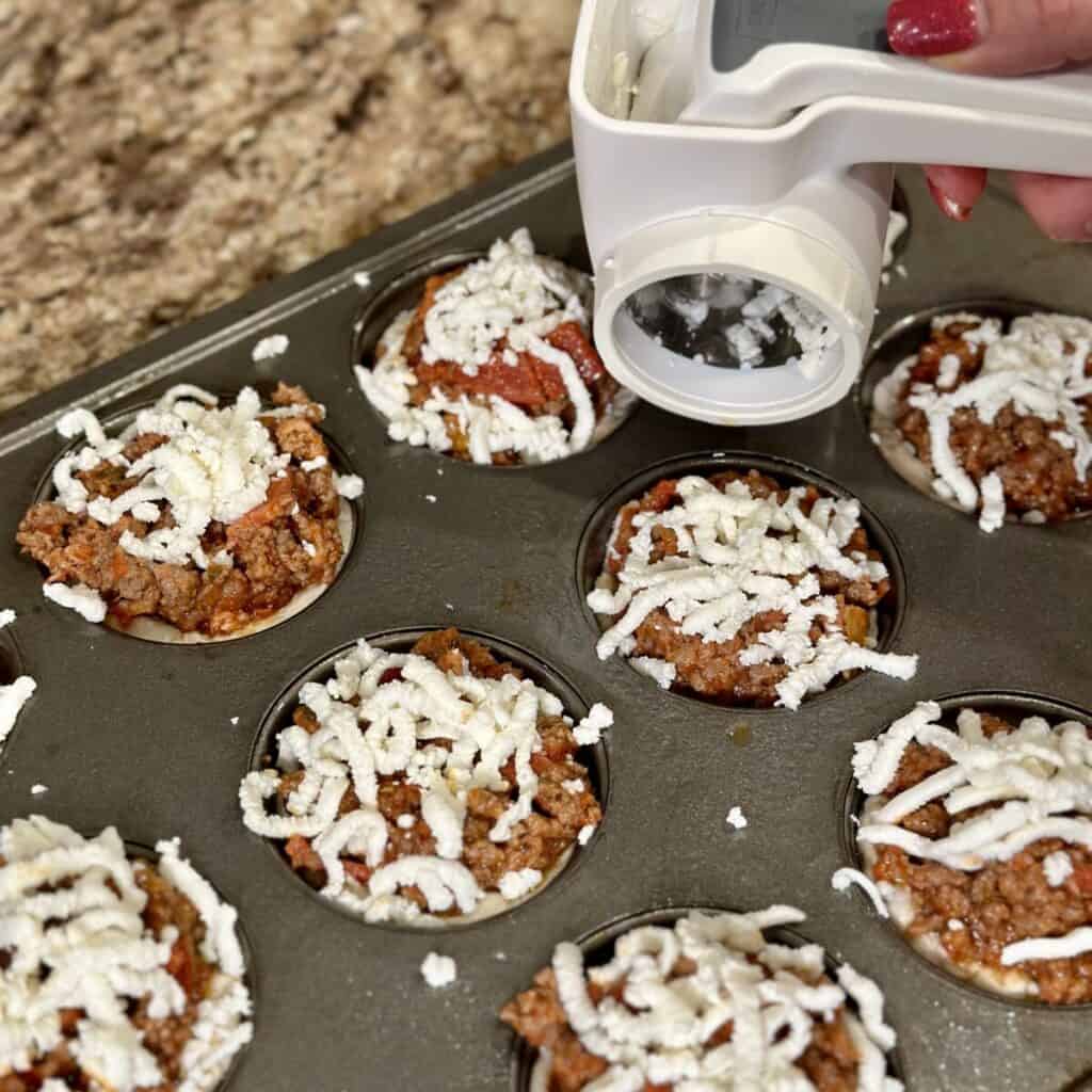 Adding cheese to the top of pizza cups.